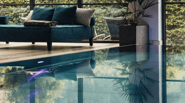 Indoorpool mit gemütlicher Doppelliege und Blick in den Hotelgarten im Wellnesshotel Nesslerhof in Großarl, Salzburger Land