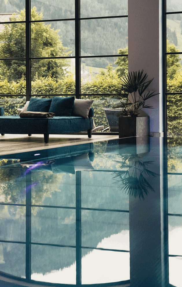 Indoorpool mit gemütlicher Doppelliege und Blick in den Hotelgarten im Wellnesshotel Nesslerhof in Großarl, Salzburger Land