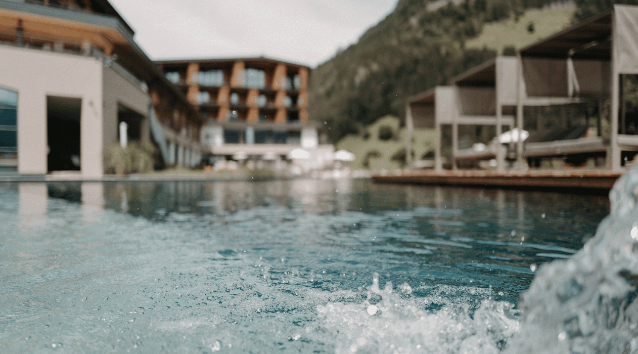 Naturschwimmteich mit kleinem Wasserfall und Lounge-Betten vor dem Wellnesshotel Nesslerhof in Großarl - the natureness hotel