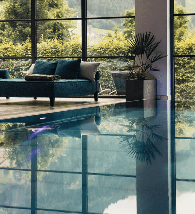 Indoorpool mit gemütlicher Doppelliege und Blick in den Hotelgarten im Wellnesshotel Nesslerhof in Großarl, Salzburger Land