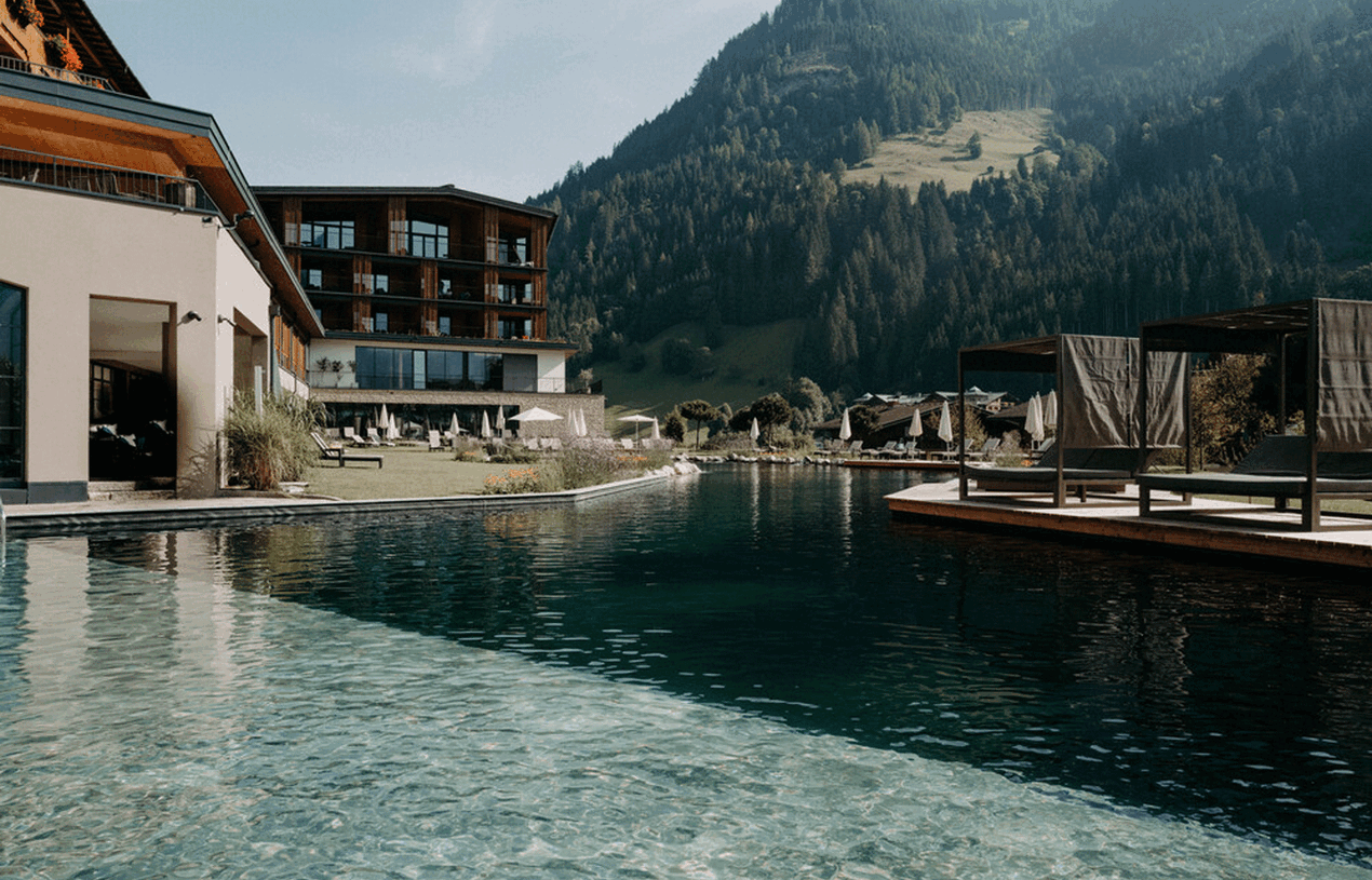 Der großzügige Naturschwimmteich mit Lounge-Betten und Sonnenschutz im luxuriösen Wellnesshotel Nesslerhof in Großarl, Salzburger Land.