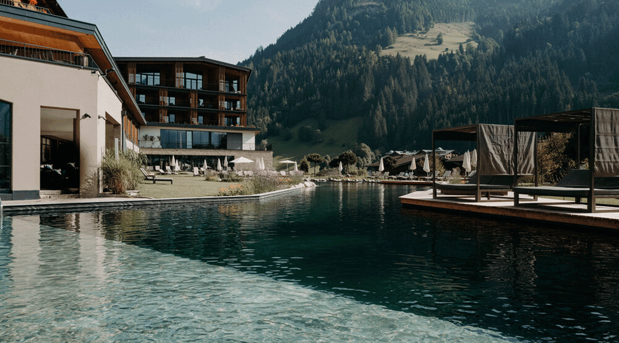 Der großzügige Naturschwimmteich mit Lounge-Betten und Sonnenschutz im luxuriösen Wellnesshotel Nesslerhof in Großarl, Salzburger Land.