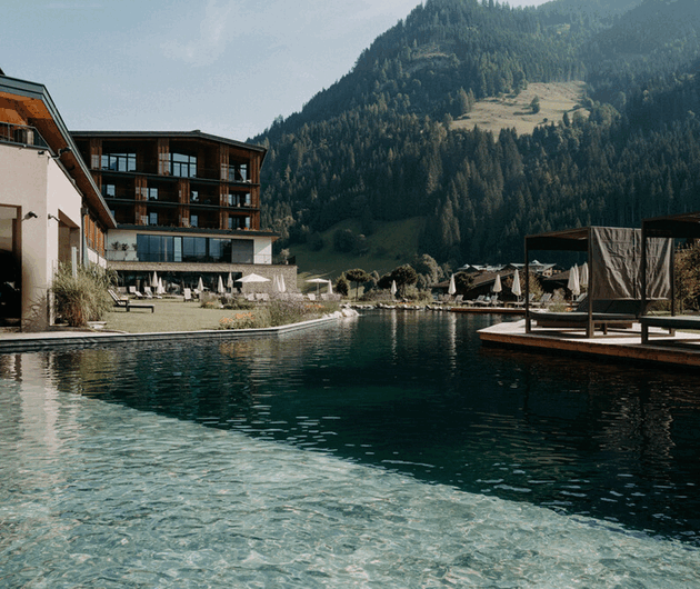 Der großzügige Naturschwimmteich mit Lounge-Betten und Sonnenschutz im luxuriösen Wellnesshotel Nesslerhof in Großarl, Salzburger Land.