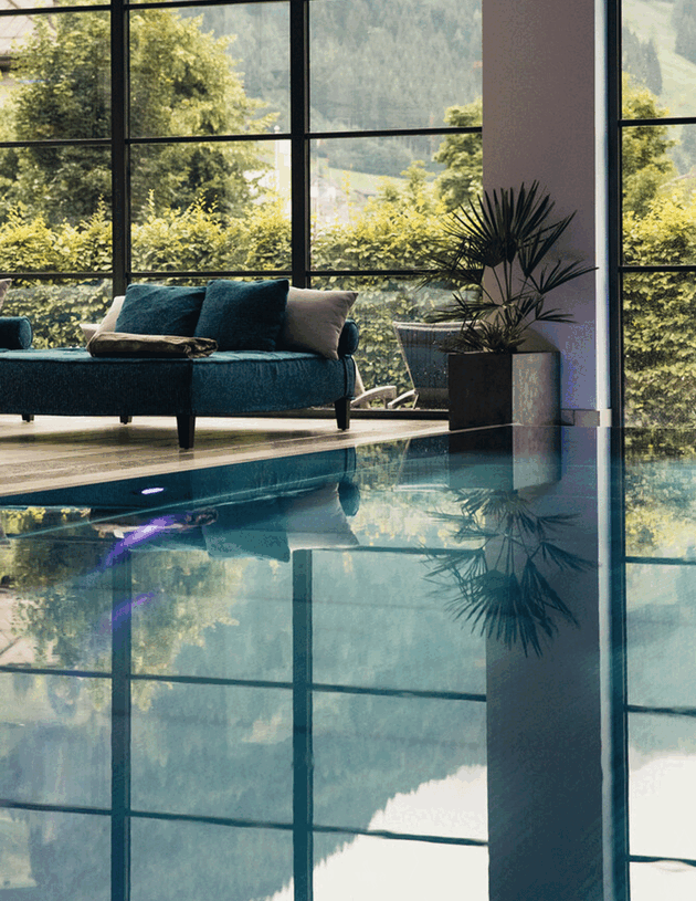 Indoorpool mit gemütlicher Doppelliege und Blick in den Hotelgarten im Wellnesshotel Nesslerhof in Großarl, Salzburger Land