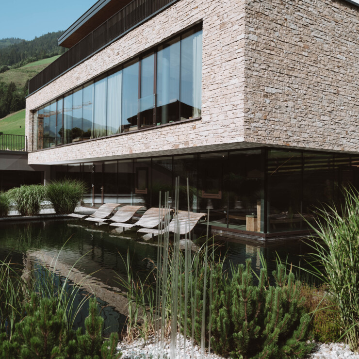 Kaltwasserpool mit schwebenden Doppelliegen aus Holz im großzügigen Garten des Wellnesshotels Nesslerhof in Großarl, Salzburger Land